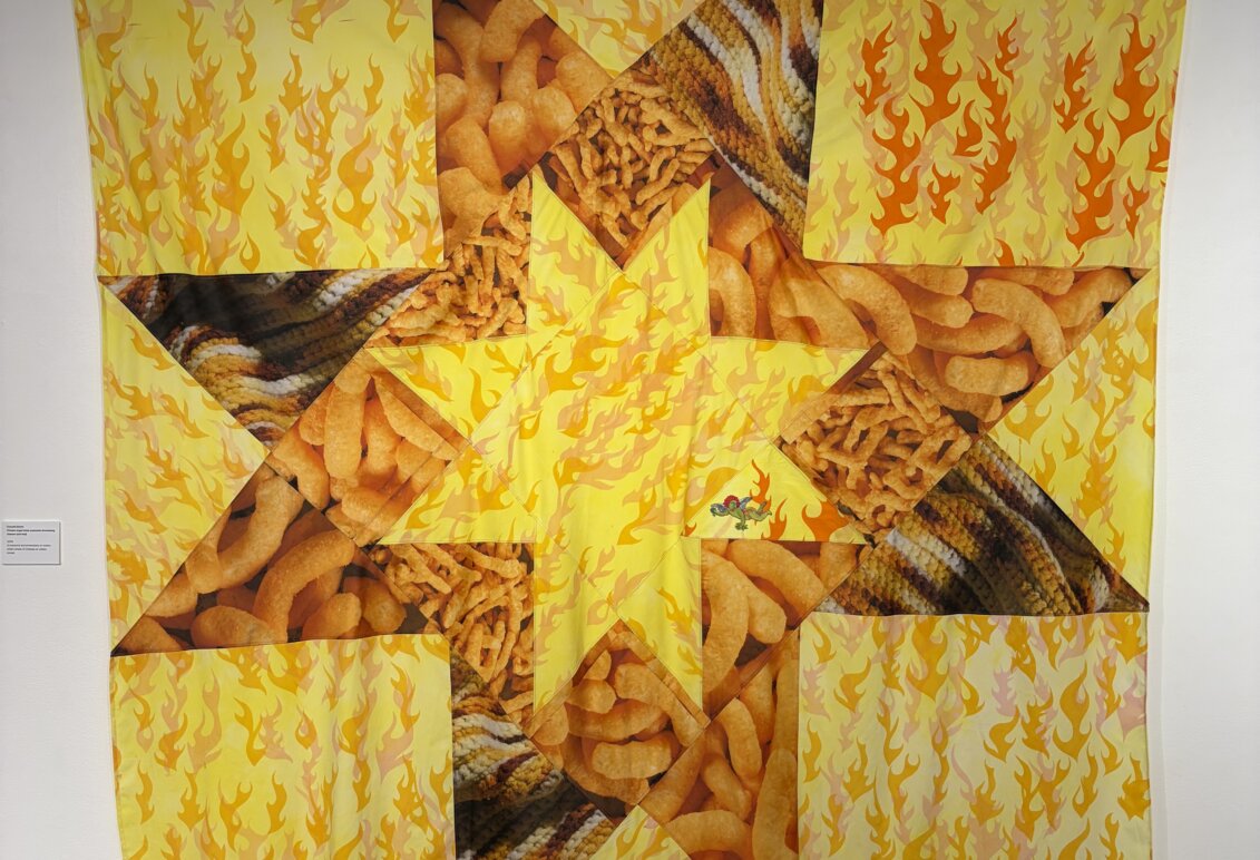 Large yellow and orange textile artwork featuring flame patterns, snack-food imagery and geometric shapes.