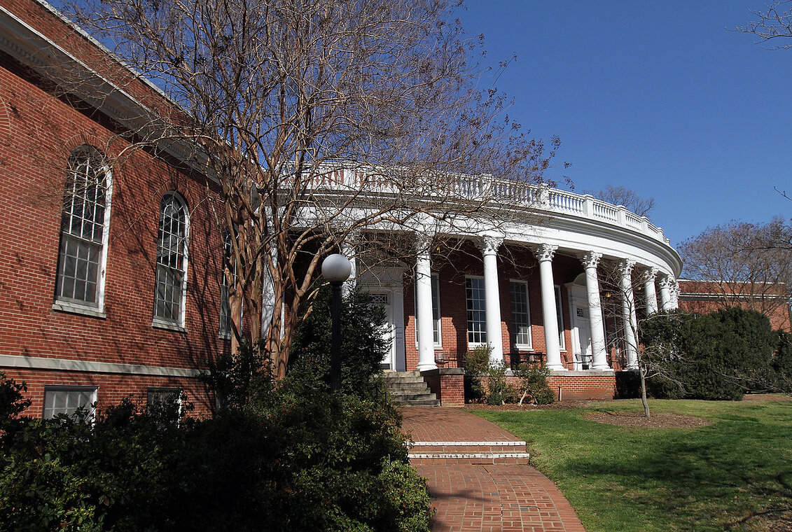 brick building with white pillars and foliage surrounding it