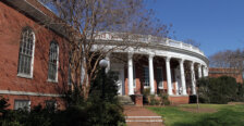 brick building with white pillars and foliage surrounding it
