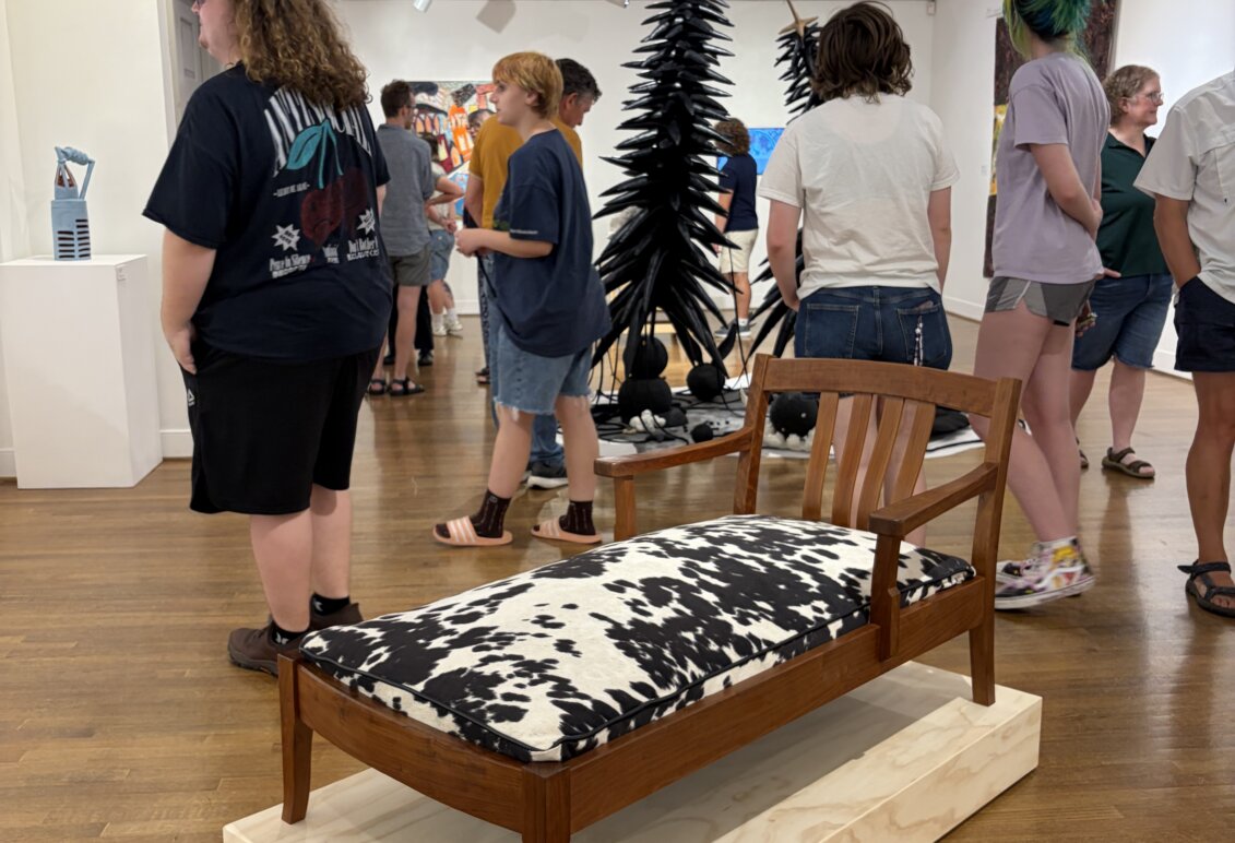 Gallery visitors move among sculptures, furniture and colorful artwork displayed throughout the exhibition space.