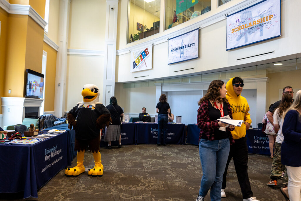 Several students and an Eagle mascot mingle in a lobby with "ASPIRE" signs on the wall