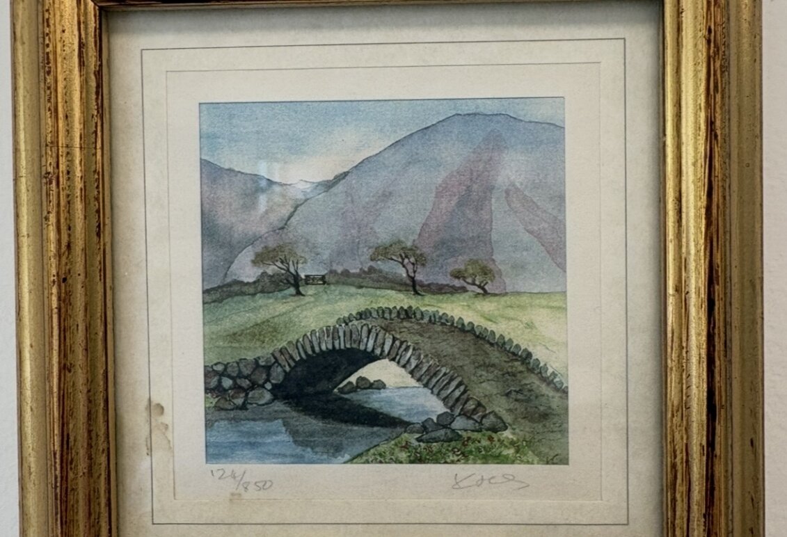 A watercolor painting of a cobblestone bridge with mountains in the backrgound