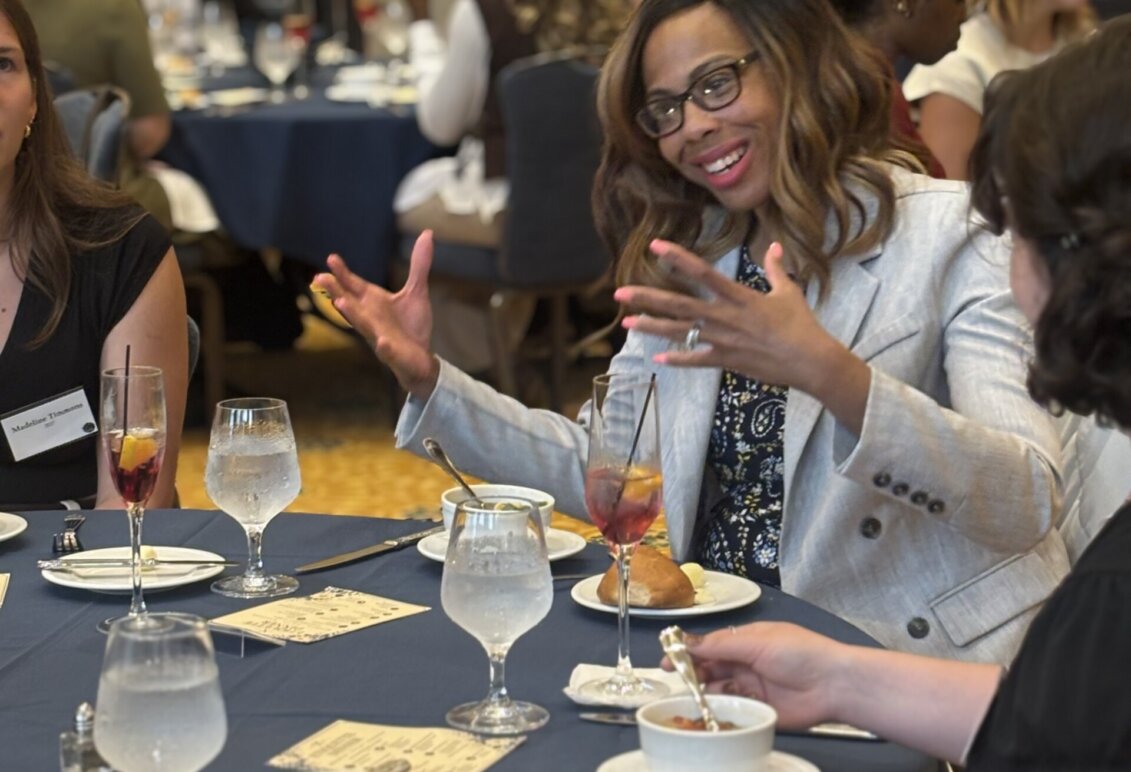 A woman uses her hands while talking and sitting at a formal dinner table