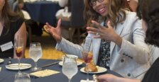 A woman uses her hands while talking and sitting at a formal dinner table