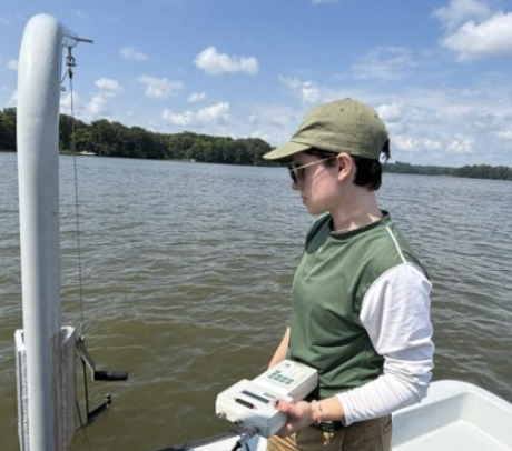A student stands in a vessel on the water while holding an electronic measuring device