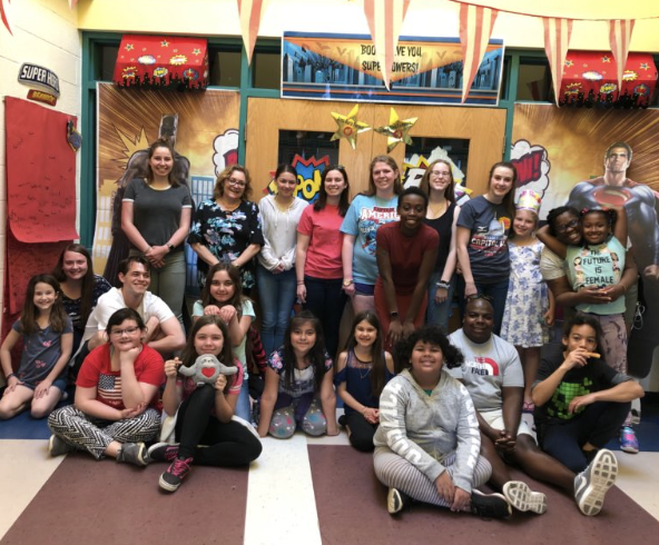 A group of college students pose with younger children inside a school