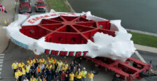 A giant piece of technology on a tractor trailer, along with a large group of people, taken from an aerial view.