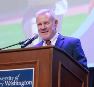 man in a jacket and tie stands behind microphone at a wooden podium at UMW