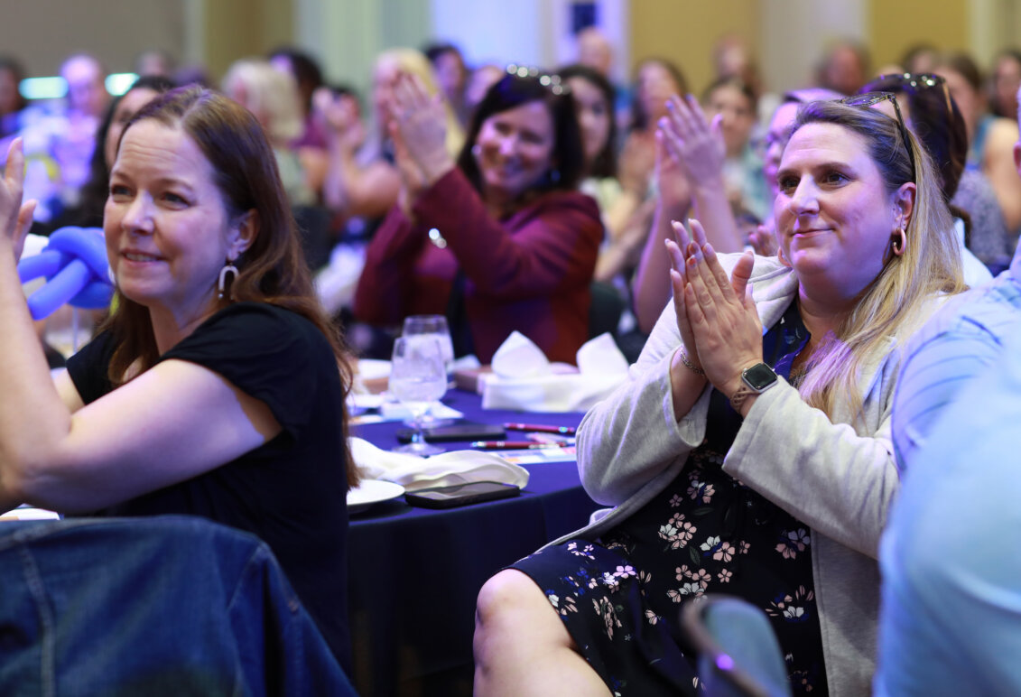 People sitting at tables in a crowded room smile and clap