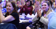 People sitting at tables in a crowded room smile and clap