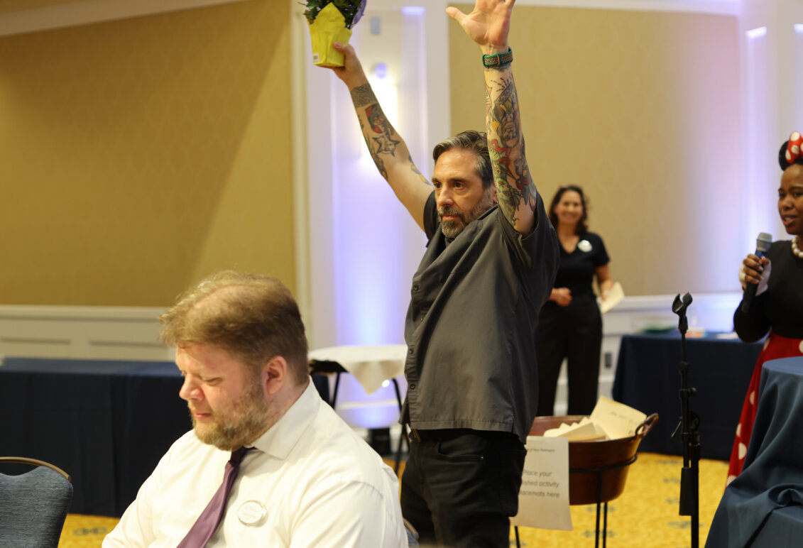 A man stands in the middle of a crowded room holding his hands in the air in a victory pose