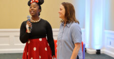A woman dressed like Minnie Mouse and holding a microphone stands beside another woman