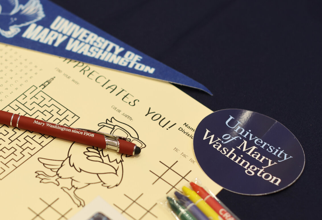 A piece of paper with a maze and other games sits on a table along with a University of Mary Washington sticker and pennant
