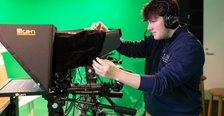 a college student in blue sweater operates a large video camera on a tripod