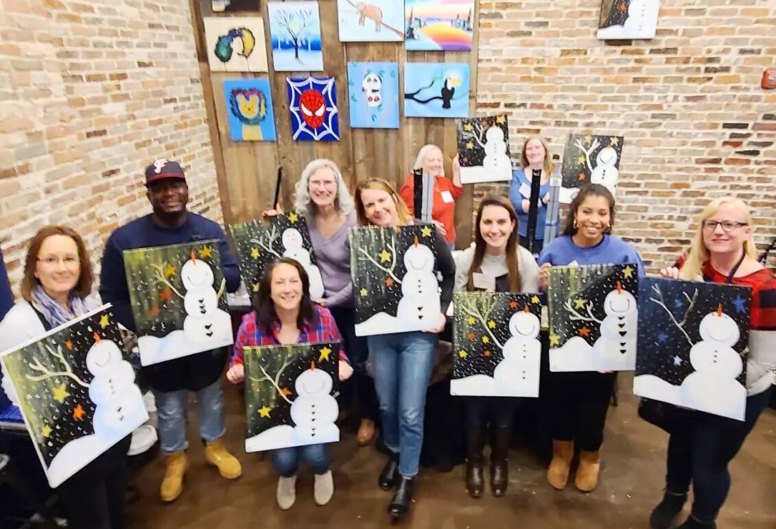 A group of people holding paintings of snowmen in a paint bar.