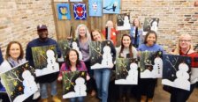 A group of people holding paintings of snowmen in a paint bar.