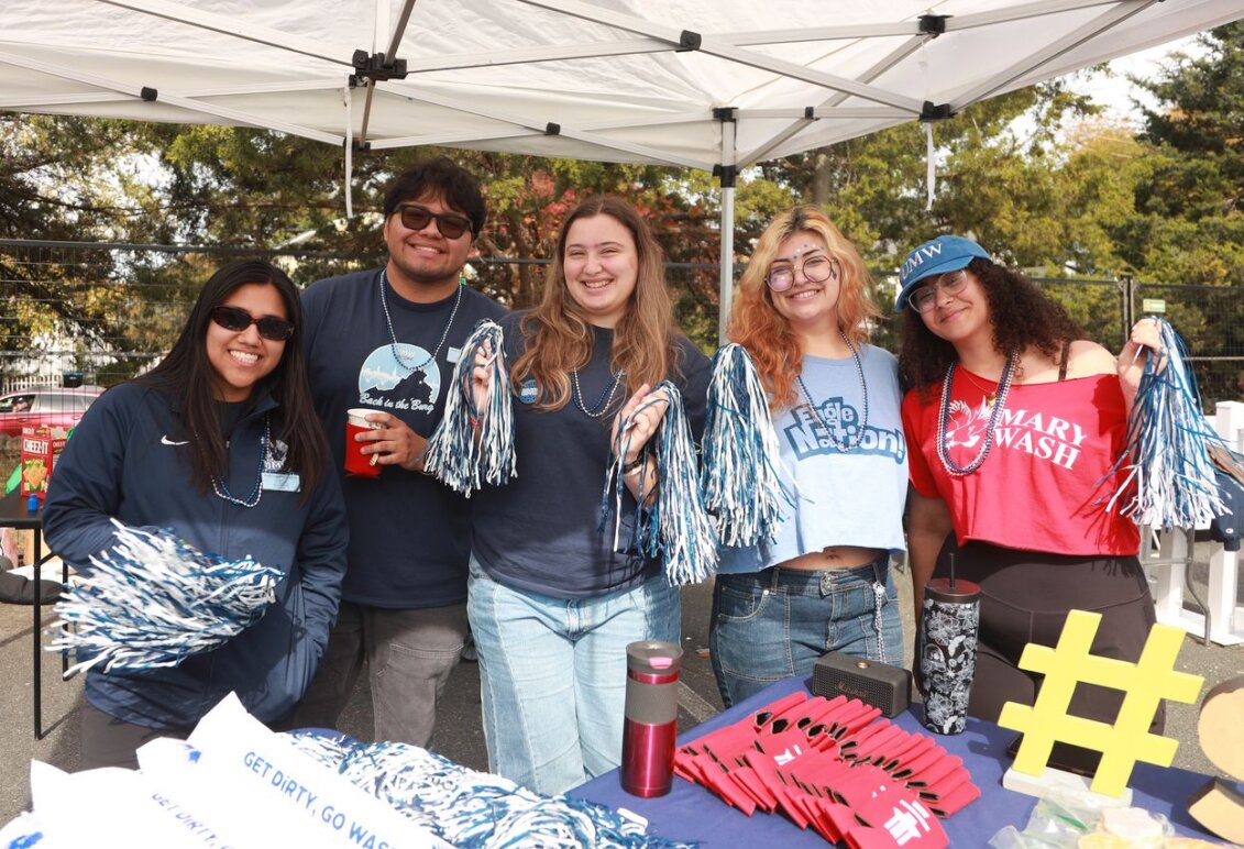 Five students hold spirit sticks behind a table displaying Mary Wash merchandise.