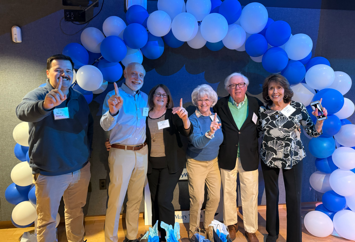 A group of six people standing under a blue and gray balloon arch.