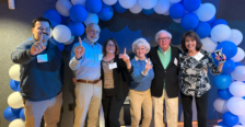 A group of six people standing under a blue and gray balloon arch.