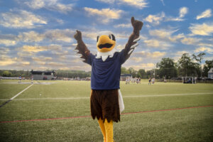 UMW eagle mascot stands outdoors at sporting event with arms raised