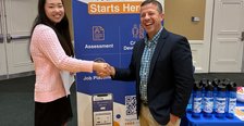 A man and a female student shake hands in front of a sign for Goodwill Industries at a Career Fair tabling event.