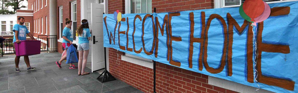 Blue banner with red writing saying Welcome Home hanging in front of Randolph Hall