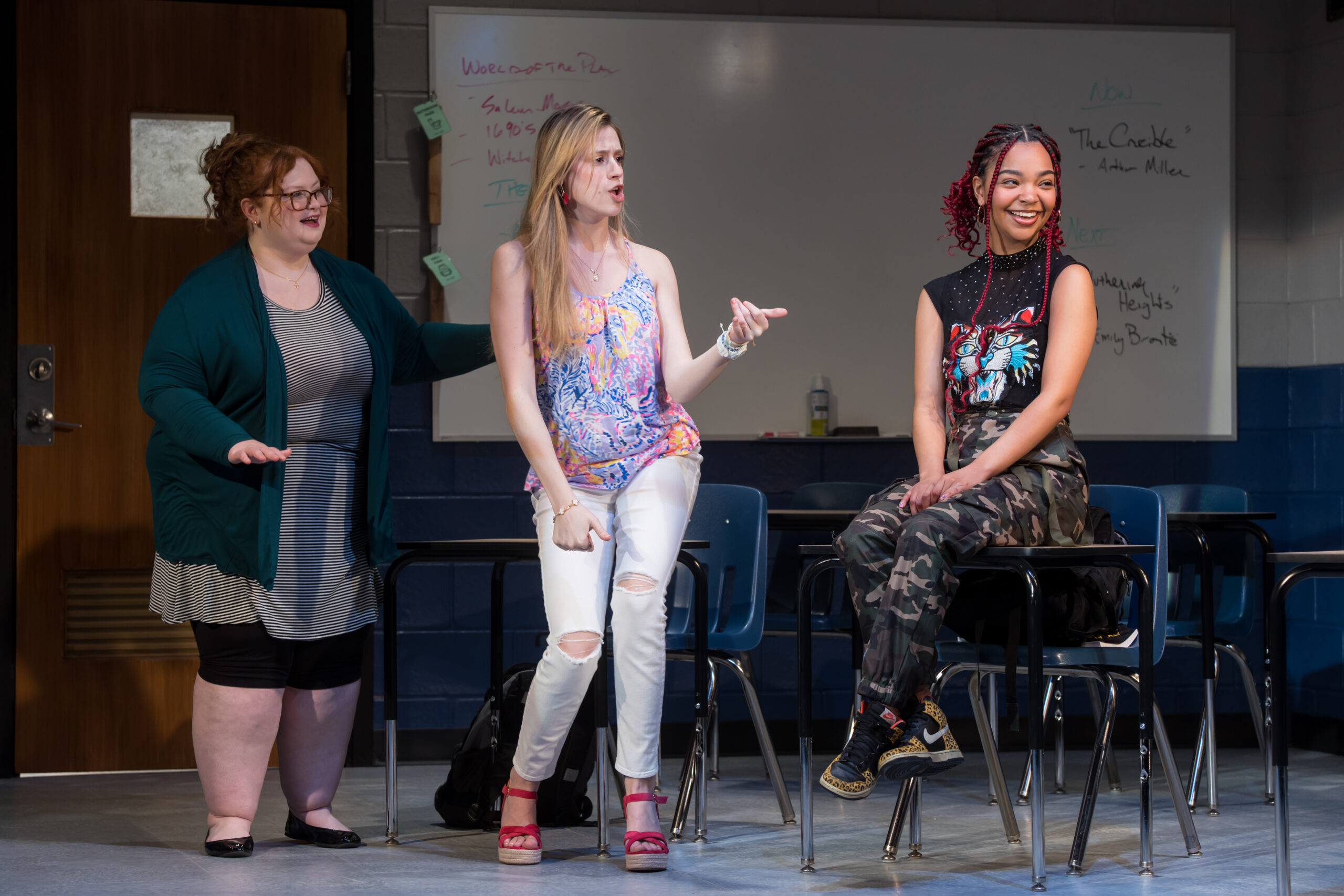 Three actors on stage in a classroom scene performing "John Proctor is the Villain".