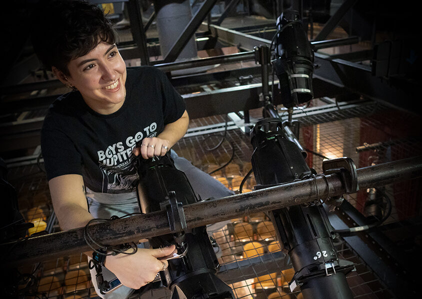 Student smiling while working on lights in the catwalk of Klein Theater.